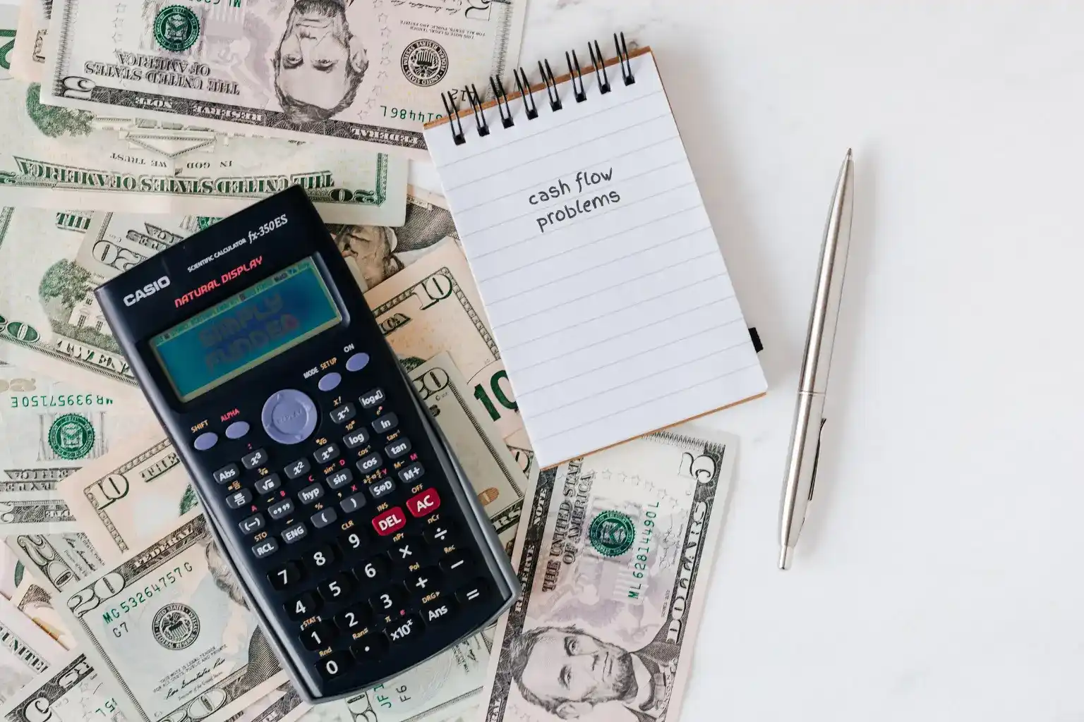 image of us dollar with casio calculator on top and a note with "cash flow written" and a stainless pen